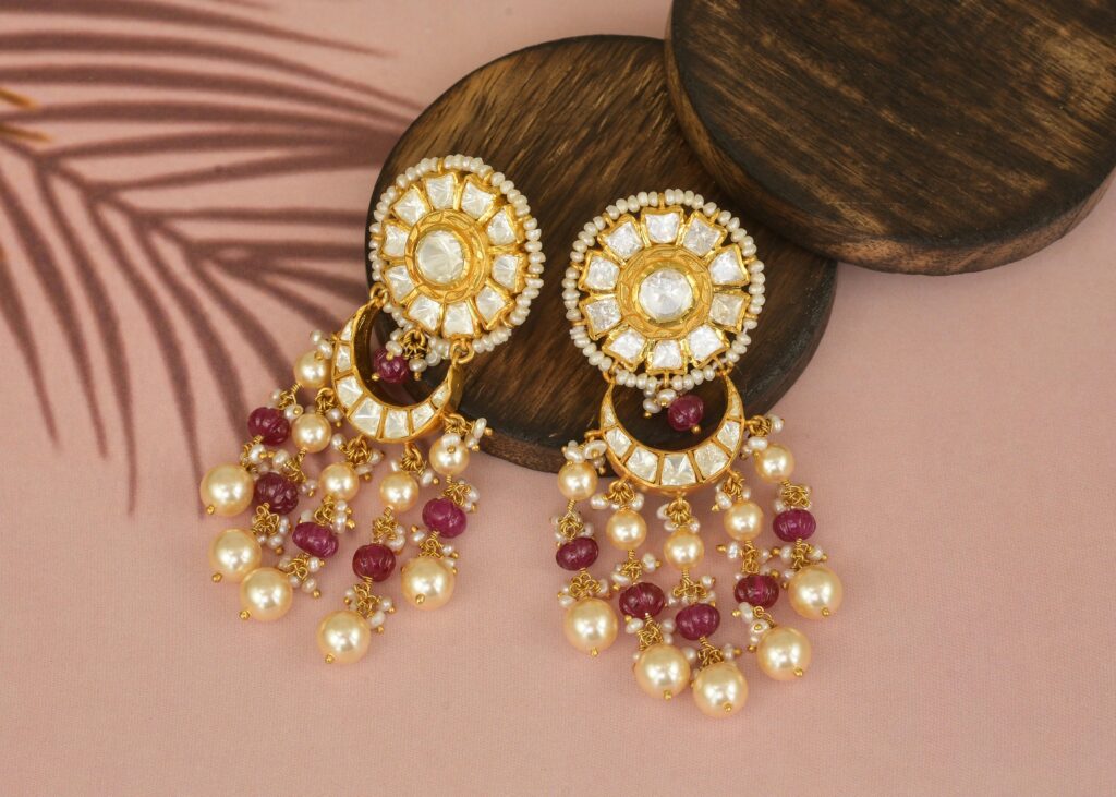 Close-up of gold and pearl earrings with gemstones on a wooden surface.